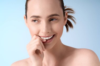 Çekici ve modaya uygun genç bir kadın, yumuşak mavi bir arka plana karşı poz verirken kendine güvenerek gülümsüyor..