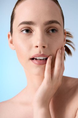 Genç bir kadın zarif bir şekilde poz veriyor, düşünceli bir şekilde yüzüne dokunuyor..