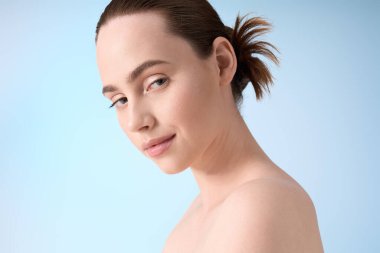 Genç bir kadın zarif bir şekilde ışıldar yumuşak mavi bir arka planda..