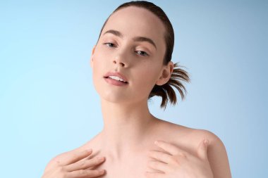 Kendine güvenen genç bir kadın zarif bir şekilde poz veriyor. Yumuşak mavi bir zemin, ışıldayan bir güzellik..