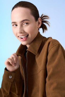 Modaya uygun genç bir kadın açık mavi bir arka planda neşeli ve stil dolu bir şekilde poz veriyor..