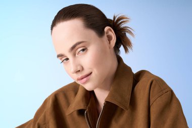 Şık bir genç kadın kendine güveni yayıyor, modern modayı yumuşak mavi bir arka plana karşı sergiliyor..