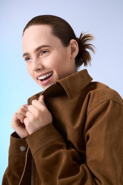 Çekici genç kadın neşeli bir gülümsemeyle modaya uygun kahverengi ceketini sergilerken neşesini gösteriyor..