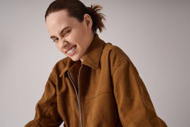 Güzel ceketli genç bir kadın minimalist bir ortamda neşeli bir gülümseme sergiliyor..