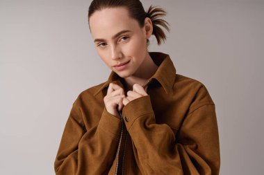 Kendine güvenen genç bir kadın, şık ceketini tarafsız bir arka plana göre ayarlar..