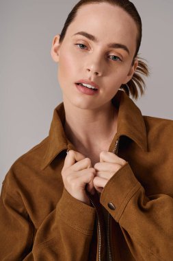 Modayı takip eden kahverengi ceketli genç kadın kendine has tarzını ve özgüvenini bir stüdyo ortamında sergiliyor..