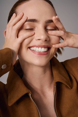 Genç ve güzel bir kadın stilini ve neşesini sergiliyor. Elleri yüzünde neşeyle gülümsüyor..