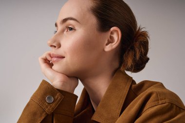 Genç ve güzel bir kadın, düşünceli bir şekilde çenesini elinin üzerinde dinlendirirken moda anlayışını sergiler..