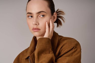 Şık giyinmiş genç ve güzel bir kadın. Minimalist bir arka planda, düşünceli bir şekilde yüzüne dokundu..