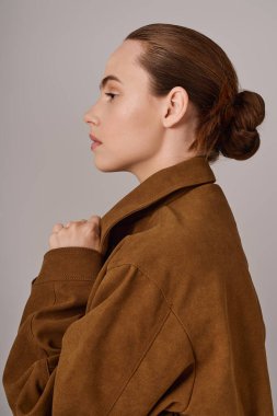 Şık, kahverengi bir ceket ve zarif bir saç stiliyle poz verirken kendine güveni tam bir genç kadın.