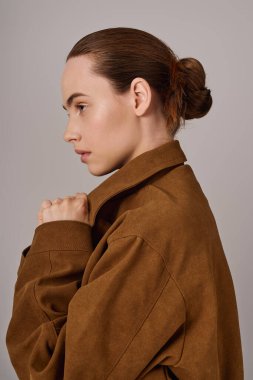 Genç bir kadın zarif moda anlayışını göstererek, ceketini tutarak kurnazca başını çevirir..