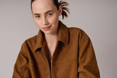 Şık bir genç kadın kahverengi ceketle poz veriyor, modern tarz ve güven yayıyor..