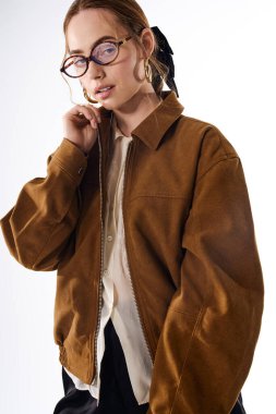 Şık bir genç kadın kendine güvenerek poz verir, şık bir ceket giyer ve zarif gözlükler takar..