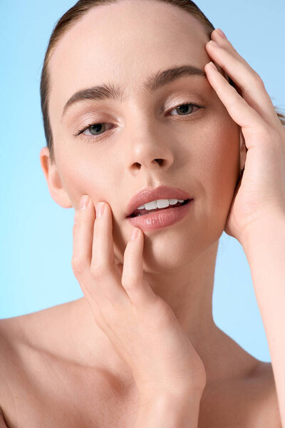 Модная женщина нежно касается своего лица, демонстрируя красоту и уравновешенность в минималистской обстановке.