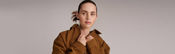 Стильная молодая женщина уверенно показывает шикарный коричневый пиджак на фоне минимализма.