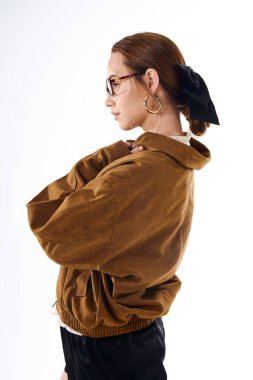 Tarz sahibi kahverengi ceketli genç bir kadın hafif bir arkaplana karşı şık bir şekilde poz veriyor..