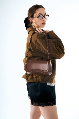 Genç bir kadın şık kıyafetlerini modern bir ortamda şık bir çantayla sergiliyor..