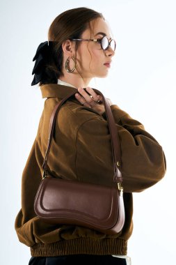 Şık bir genç kadın, kendine has moda anlayışını şık bir el çantası ve klasik gözlüklerle sergiliyor..