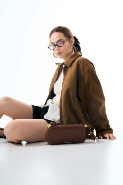 Şık genç kadın, şık kıyafetler ve parlak ışıkta şık aksesuarlarla zahmetsizce poz veriyor..