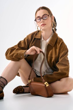 Genç bir kadın zarif kıyafetini ve çantasını temiz bir arkaplanda sergiliyor..