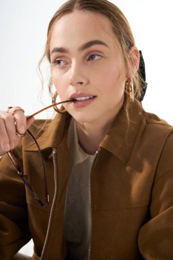 Genç bir kadın neşe içinde elinde gözlük tutarken kendine güvenir, modaya uygun kıyafetler giyer..