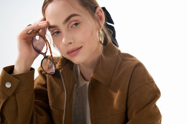 Şık bir genç kadın şık bir şekilde poz veriyor. Elinde şık gözlükler, kendine güveni ve cazibesi var..