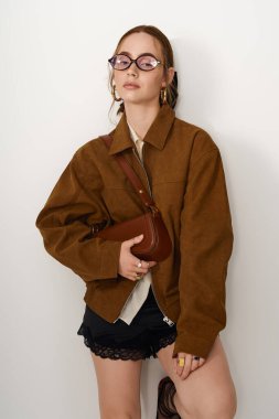 Şık, genç bir kadın şık kıyafetini sergileyerek minimalist bir arkaplanda poz veriyor..