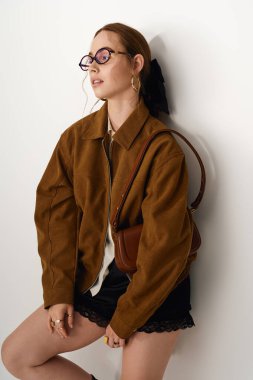 Modaya uygun genç bir kadın şık kıyafetlerini ve kalın aksesuarlarını sergileyerek zarif bir şekilde ayakta duruyor..