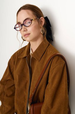 Genç bir kadın modaya uygun kahverengi bir ceket ve gözlüklerle zarafet saçıyor..