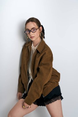 Moda kıyafetli genç bir kadın duvara yaslanıyor, kendine güveni ve çekiciliği var..