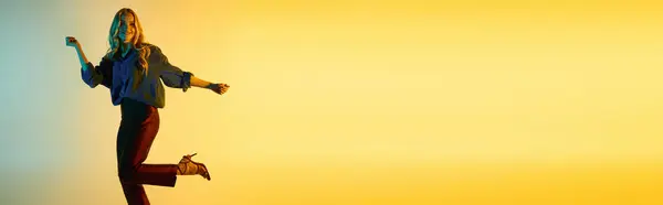 Молода жінка в модному вбранні танцює радісно на тлі барвистого фону на заході сонця. — стокове фото