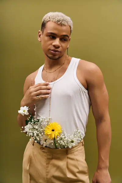 Handsome young man poses confidently in a tank top adorned with fresh flowers, exuding fashion. — Stock Photo