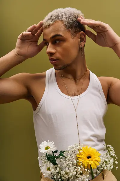 Jeune homme pose en toute confiance dans un débardeur élégant entouré de belles fleurs à l'intérieur. — Photo de stock
