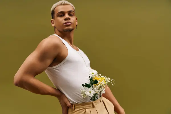 En un estudio vibrante, un joven con estilo muestra su camiseta de moda mientras sostiene flores. — Stock Photo