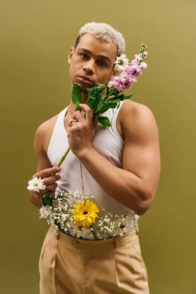 A stylish young man with dyed hair poses with vibrant flowers, exuding modern fashion in a studio. — Stock Photo