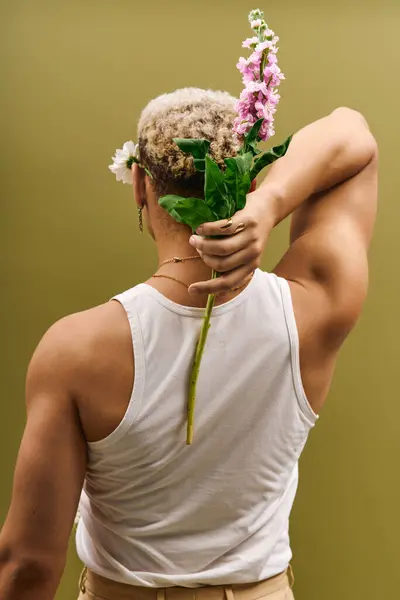 A handsome young man showcases his trendy style in a tank top holding flowers in a studio. — Stock Photo