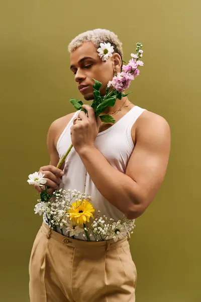 Ein junger afrikanisch-amerikanischer Mann posiert selbstbewusst mit Blumen in einem stilvollen Studio und versprüht Charme. — Stockfoto