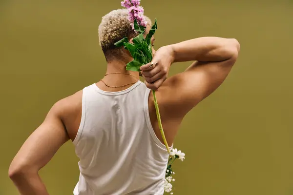 Un joven de moda exhibe un cabello teñido único mientras sostiene flores vibrantes en un estudio. - foto de stock