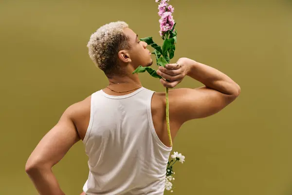 A young African American man flaunts his fashion sense in a tank top, posing with flowers. — Stock Photo
