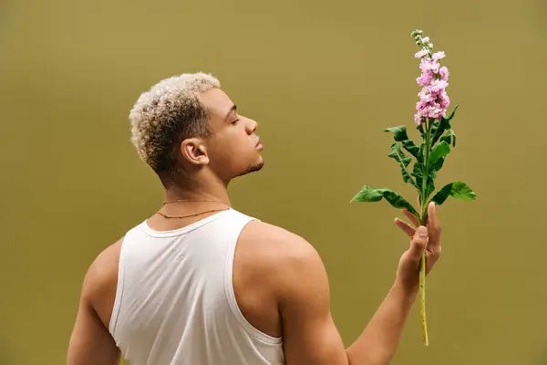 Un joven afroamericano muestra su estilo moderno mientras sostiene flores en un estudio. — Stock Photo