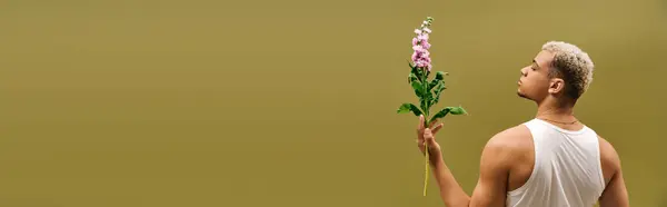 This young man poses confidently in a tank top, holding flowers against a soft background, banner — Stock Photo