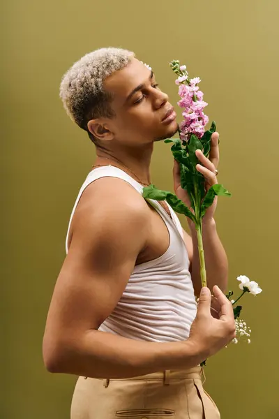 A confident young african american man poses in a tank top, holding flowers in a studio. — Stock Photo