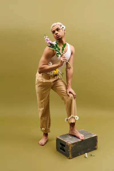 Guapo joven afroamericano posa a la moda con flores mientras muestra su estilo. - foto de stock