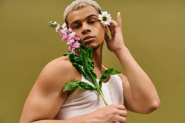 Un jeune et élégant Afro-Américain pose en toute confiance avec des fleurs dans un studio dynamique. — Photo de stock