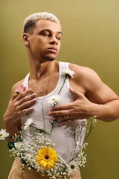A young man with dyed hair poses confidently in a tank top, adorned with flowers, in a studio. — Stock Photo