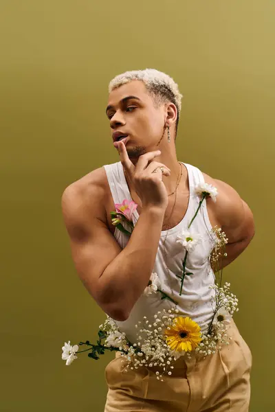 Stylish young man poses gracefully with flowers adorning his tank top in a vibrant studio. — Stock Photo