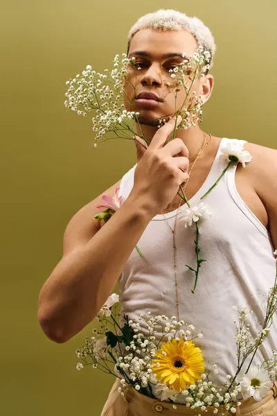 Stylish young man poses confidently among flowers in a creative studio setting. — Stock Photo