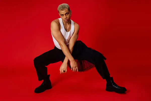 A young man exudes confidence in a tank top and black pants, posing amid a vivid red backdrop. — Stock Photo