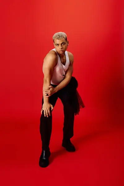 A confident young African American man showcases fashion in a striking red studio with dyed hair. — Stock Photo