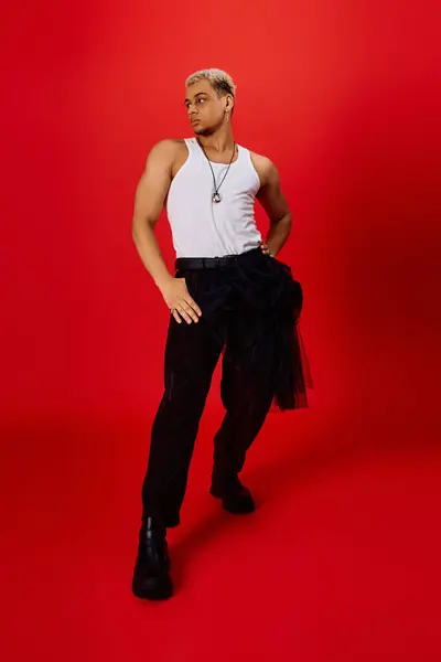 Un jeune homme afro-américain élégant modélise à la mode dans un studio rouge, rayonnant de confiance. — Stock Photo